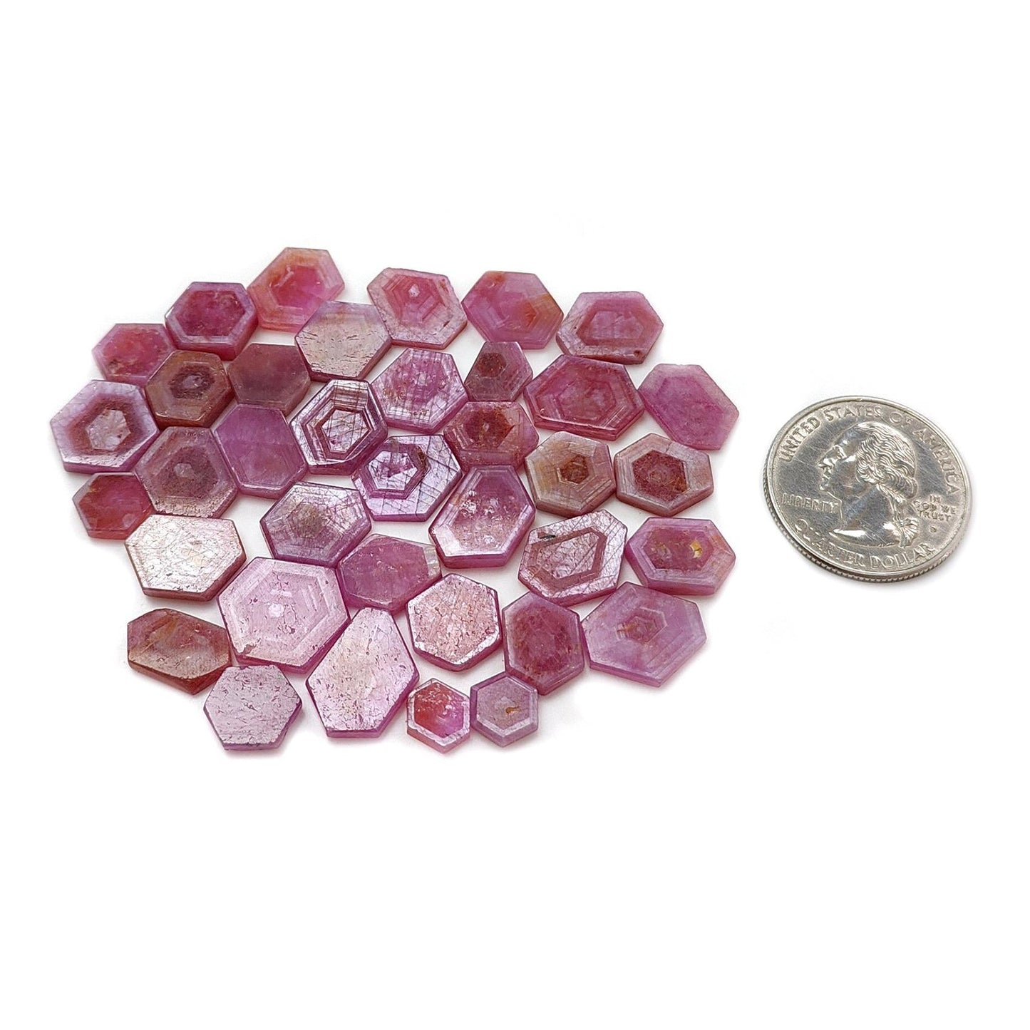 Hexagonal pink gemstones with a quarter coin for scale on a white background